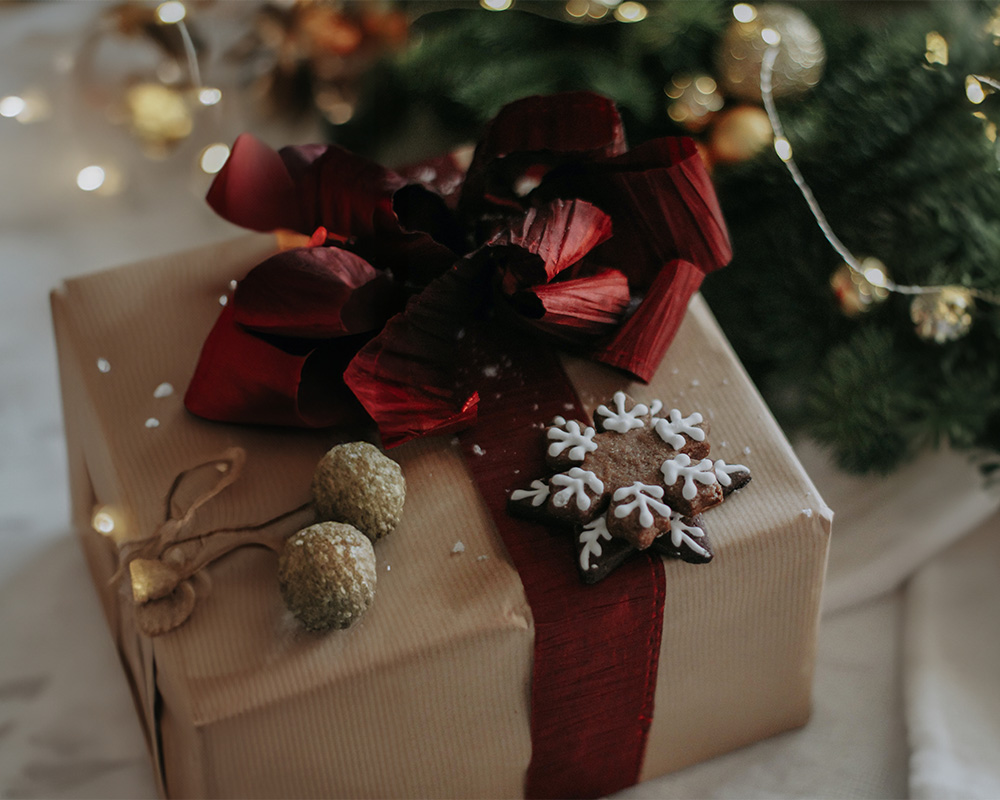 Božično darilo, zavito v papir, zavezano z metuljčkom in okrašeno s piškotom.