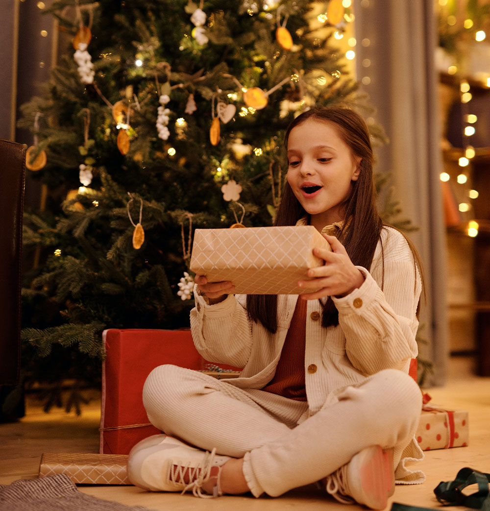 Dekle uživa v darilu pod božičnim drevesom.