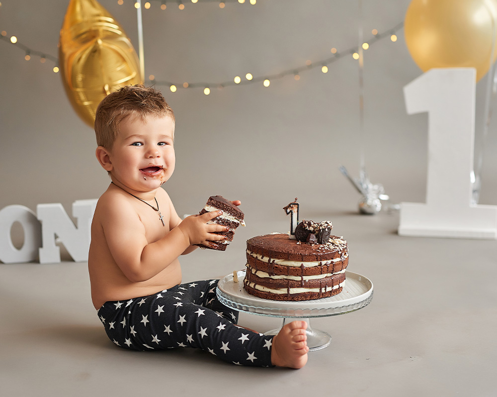 Enoletni deček ob praznovanju rojstnega dne v rokah drži kos čokoladne torte