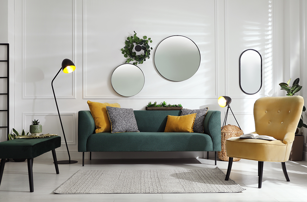 Moderna dnevna soba v svetlih barvah z zeleno zofo, rumenimi blazinami in okroglimi ogledali na steni.