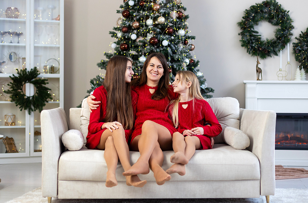 Mama in njene hčere v rdečih oblekah skupaj preživljajo praznični čas ob božičnem drevesu.