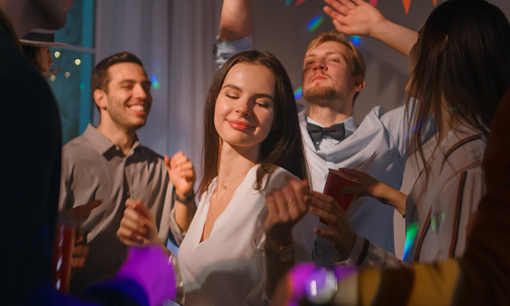 Skupina ljudi pleše na zabavi, med njimi je ženska, ki uživa v glasbi.